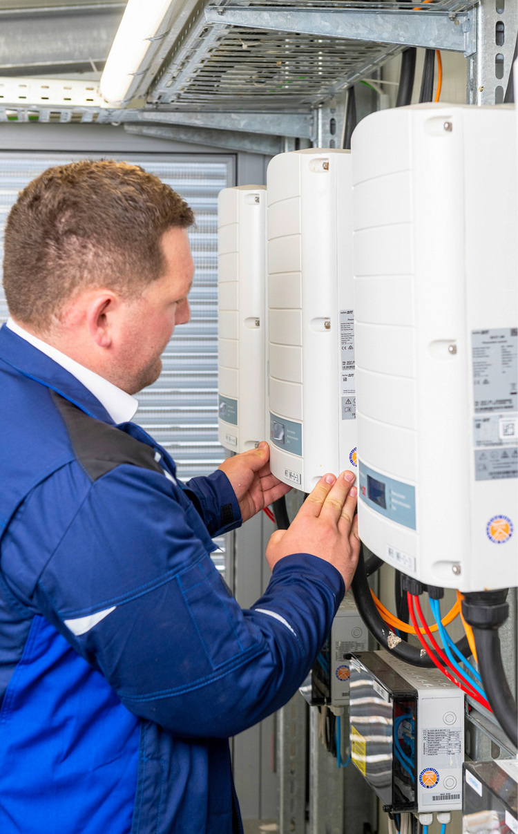 Techniker in blauer Uniform justiert an einer Wand montierte elektrische Geräte.