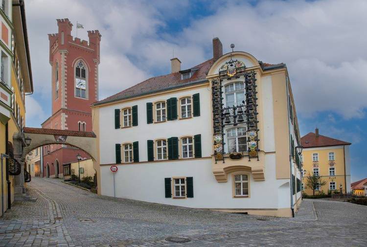 Historische europäische Straße mit einem Turm, einem reich verzierten Gebäude und einer Kopfsteinpflasterstraße unter einem bewölkten Himmel.