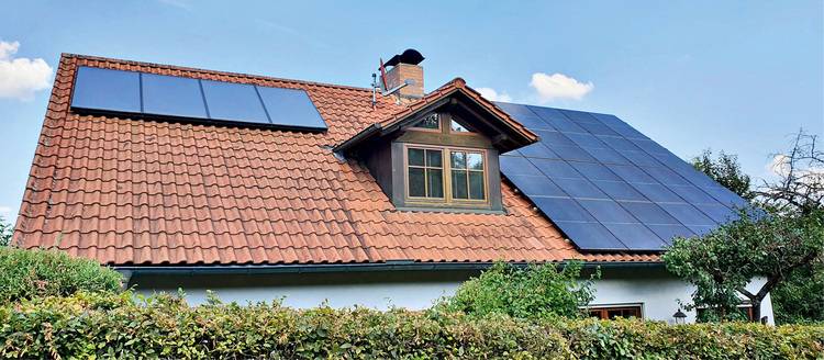 Ein Haus mit roten Dachziegeln und Solarmodulen, umgeben von Grün und einem klaren Himmel.