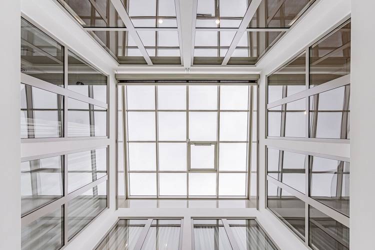 Blick nach oben auf ein modernes Atrium mit großen Glasfenstern und einer Gittermusterdecke.