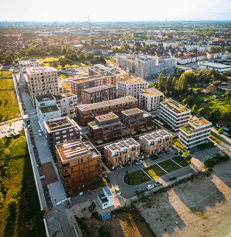 Luftaufnahme eines modernen Wohnviertels mit Grünflächen und einer Stadtlandschaft im Hintergrund.