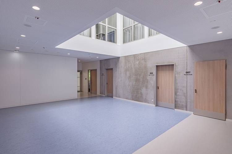 Modernes, minimalistisches Gebäudeinterieur mit blauen und weißen Böden, Holztüren und einem Oberlichtdach.