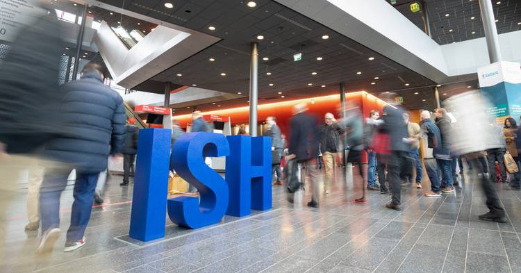 Menschen, die in einem geschäftigen, modernen Lobbybereich an einem großen blauen „ISH“-Schild vorbeigehen.