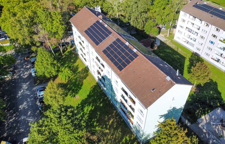 Vogelperspektive auf ein modernes Bürogebäude mit Photovoltaikanlage auf dem Dach, eingebettet in eine grüne Umgebung. Das Bild verdeutlicht die Integration erneuerbarer Energien in urbanen Gebieten für nachhaltige Gebäudetechniklösungen.