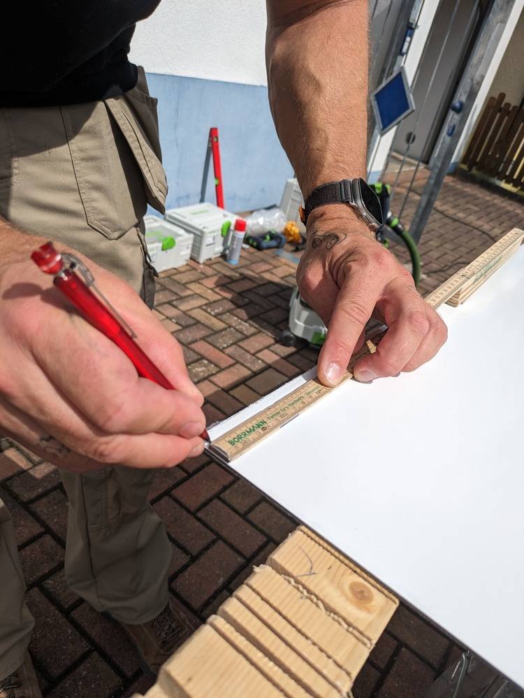 Person, die an einem sonnigen Tag Holz mit einem Lineal und einem Rotstift misst und markiert.