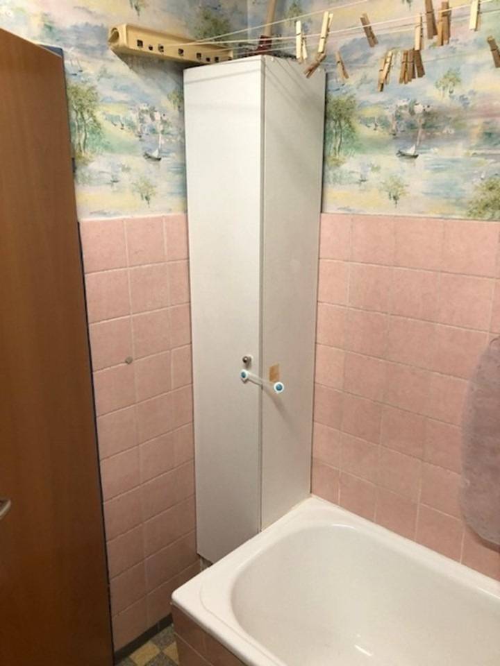 Kleines Badezimmer mit Badewanne, hohem weißen Schrank, rosa gefliesten Wänden und tapeziertem oberen Bereich.