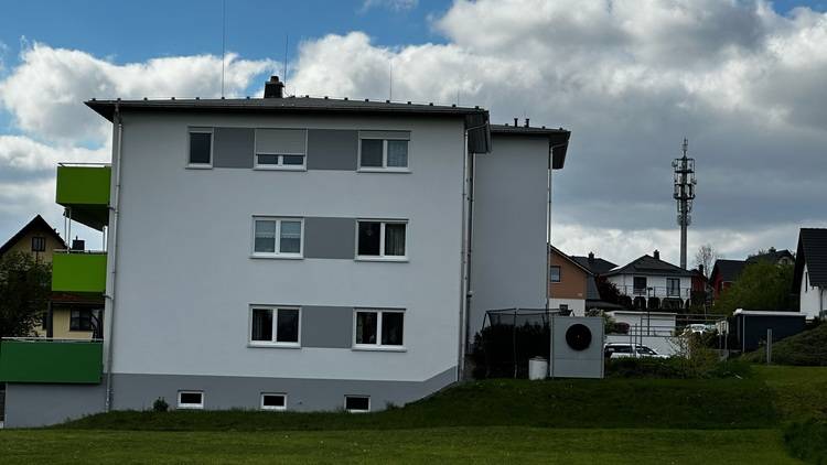 Alt-Text: „Mehrgeschossiges Wohngebäude mit energieeffizienter Fassade und integrierten grünen Balkonen, symbolisiert nachhaltige Bauweise und moderne Gebäudetechnik in Vorstadtumgebung.