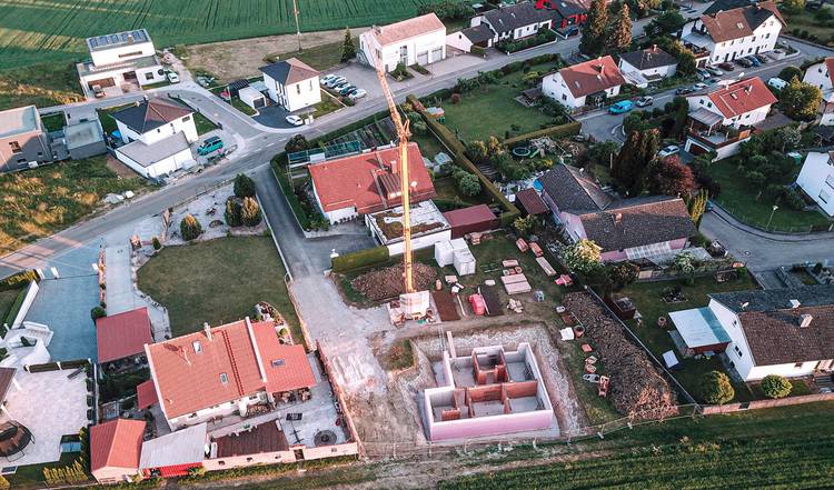 Alt-Text: „Luftaufnahme eines Wohngebiets mit installierten Solaranlagen auf den Dächern und einer nahegelegenen Baustelle für ein energieeffizientes Passivhaus mit Kran.“.