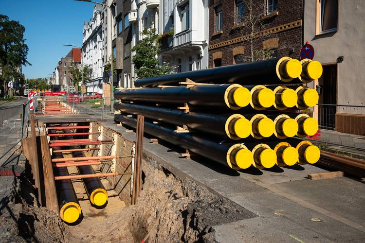 Alt-Text: „Baustelle in der Gebäudetechnik mit offenem Graben und gestapelten großen Rohren mit gelben Kappen für die Installation von Erdwärmeleitungen.