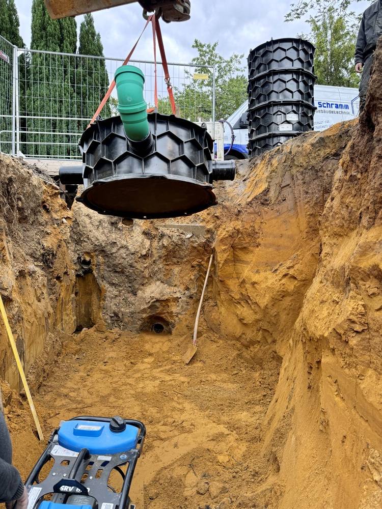 Bauarbeiten zur Installation eines Regenwassersammelsystems: Ein Kran senkt ein großes zylindrisches Modul in eine vorbereitete Baugrube. Umgeben von Werkzeugen und technischer Ausrüstung, um nachhaltige Wasserlösungen für Gebäudetechnikprojekte zu implementieren.