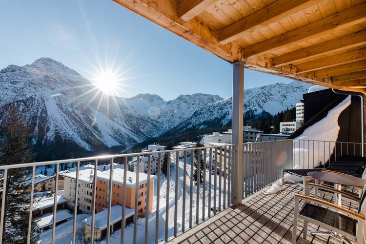 „Ein modern gestalteter Balkon mit Sitzgelegenheiten bietet einen weiten Ausblick auf energieeffiziente Gebäude und ein innovatives Heizsystem in einer verschneiten Berglandschaft, symbolisiert den Fortschritt in der thermischen Optimierung und nachhaltigen Gebäudetechnologie bei klarem, sonnigem Wetter.