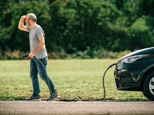 Mann hält Ladekabel in der Hand und sucht nach Ladesäule oder Ladestation für Elektroauto