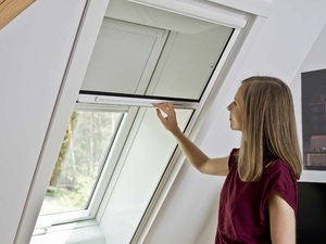 Roto Insektenschutzrolle an einem Dachfenster mit einer Frau davor, die es bedient